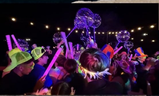Multidão na pista com pulseiras neon e perucas coloridas
